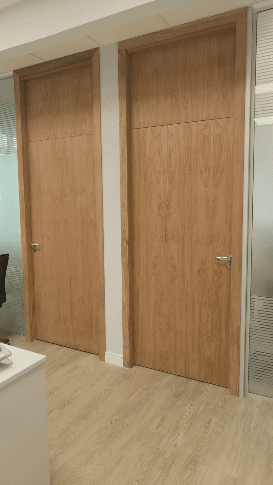 Duas portas amadeiradas com bandeiras superiores em um ambiente com divisórias de vidro