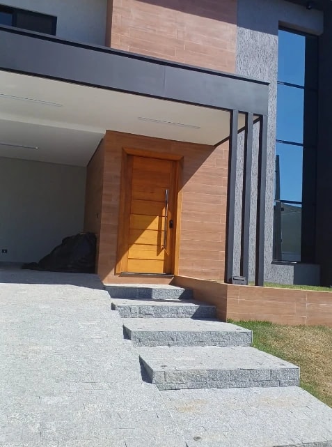 Porta de madeira fechada na entrada de uma casa com degraus e revestimento amadeirado ao redor.