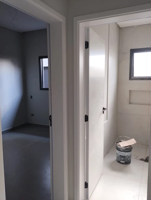 Porta branca entreaberta com paredes e piso claros.