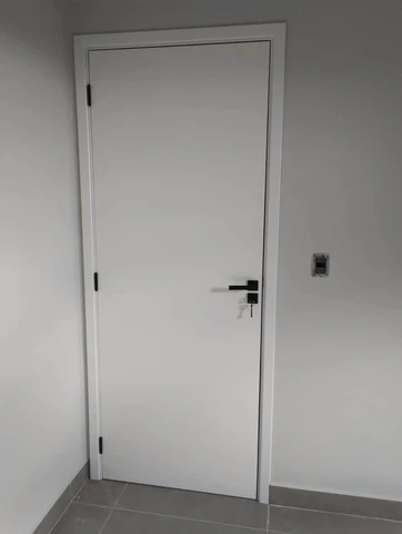 Porta branca fechada com maçaneta escura e piso cinza.