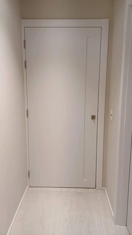 Porta branca com frisos, moldura clara e maçaneta metálica.