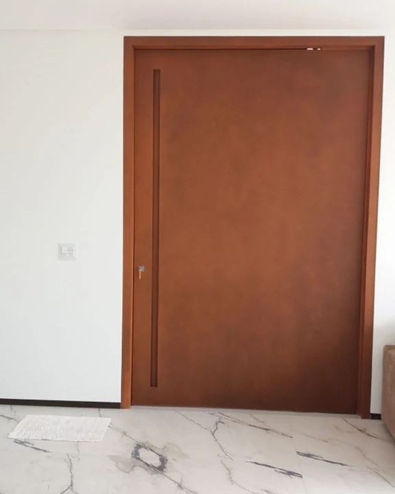 Porta em tom ferrugem com cava vertical e piso claro.