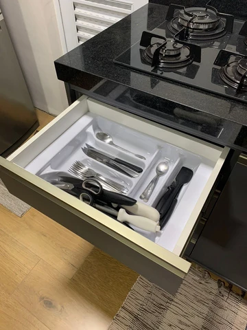 Gaveta de cozinha aberta com organizador de talheres sob uma bancada escura.