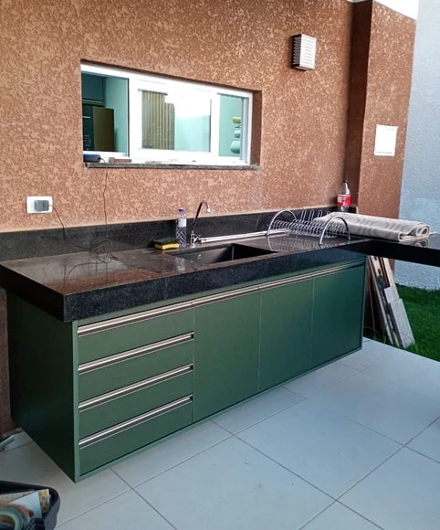 Gabinete verde com gavetas e portas sob uma pia de bancada escura.