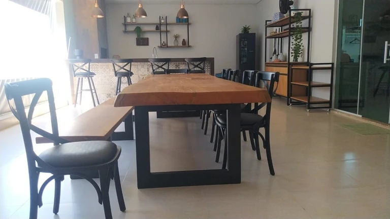 Mesa e banco de aparência amadeirada com bases pretas em sala de jantar integrada a um balcão.