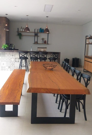 Vista longitudinal de mesa de aparência amadeirada com fruteira, banco e cadeiras pretas.