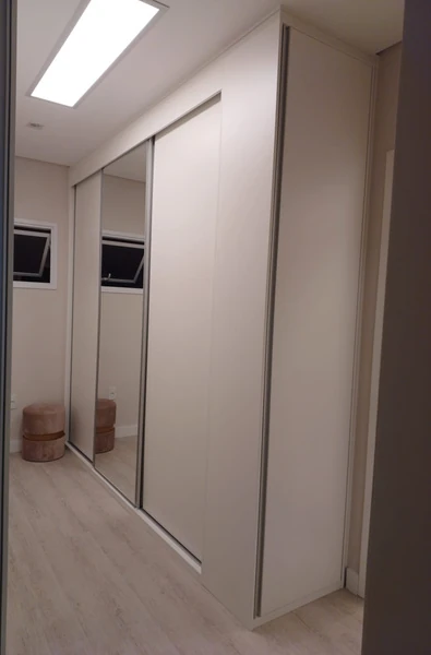 Armário de portas claras e espelhadas ocupando uma parede de corredor.